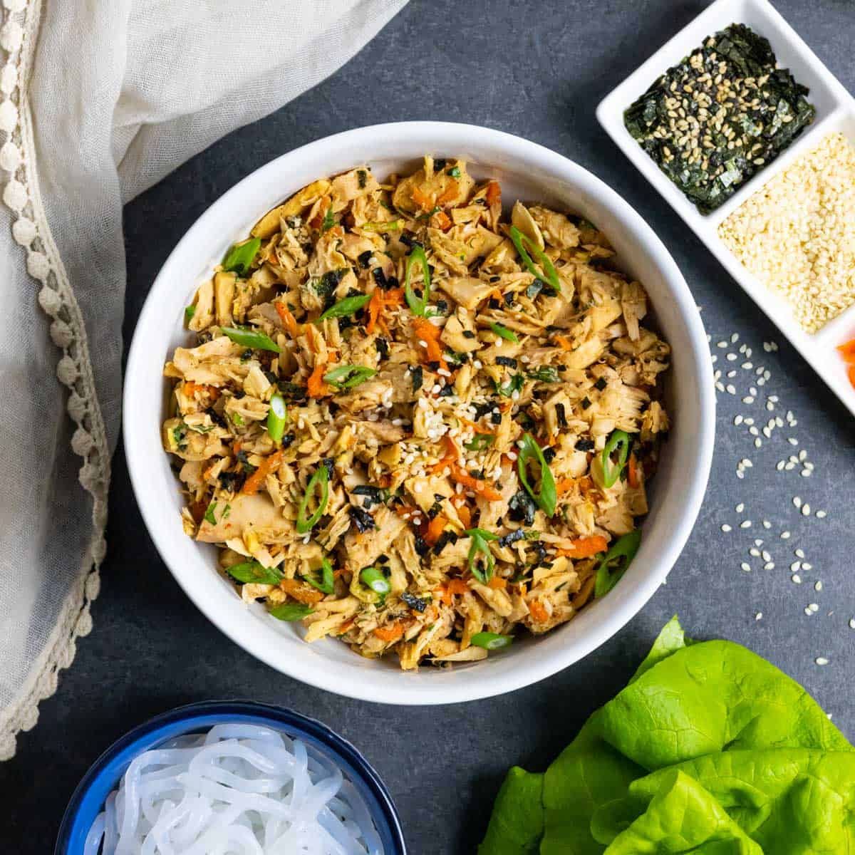 Low-FODMAP Asian style tuna salad with sliced green onions in a white bowl with shirataki noodles and butter lettuce on the side.