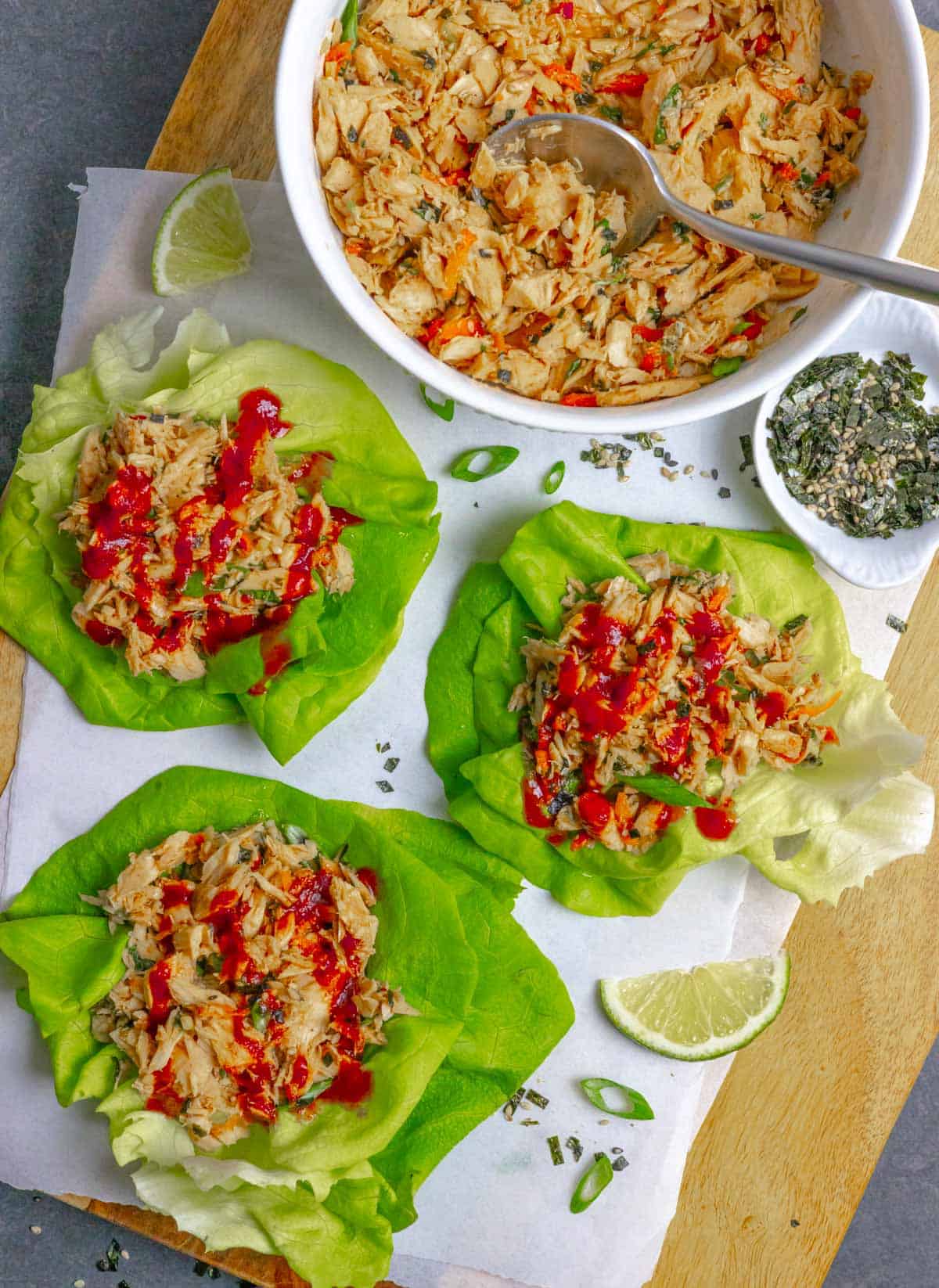 Three bright green butter lettuce leaf wraps with finished salad and sriracha sauce on top on a board.