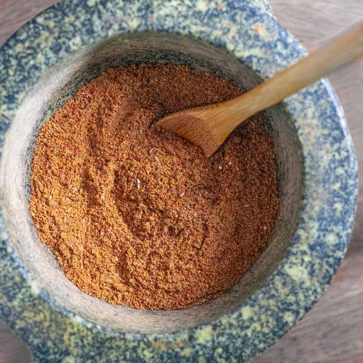 Pulled pork barbecue rub in a granite mortar with a small wooden spoon in the bowl.