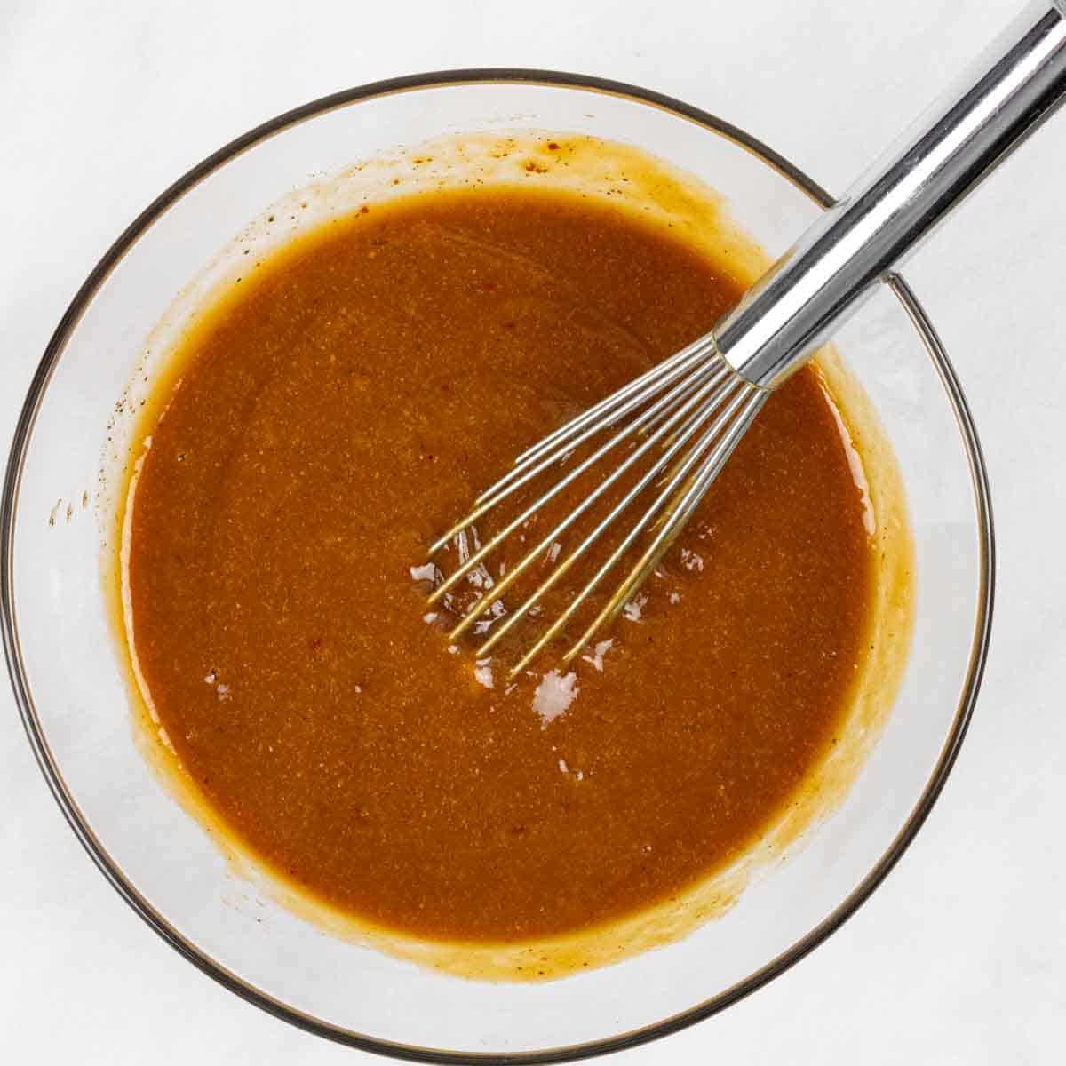 White bowl of barbecue sauce mixed, with a whisk in the bowl.
