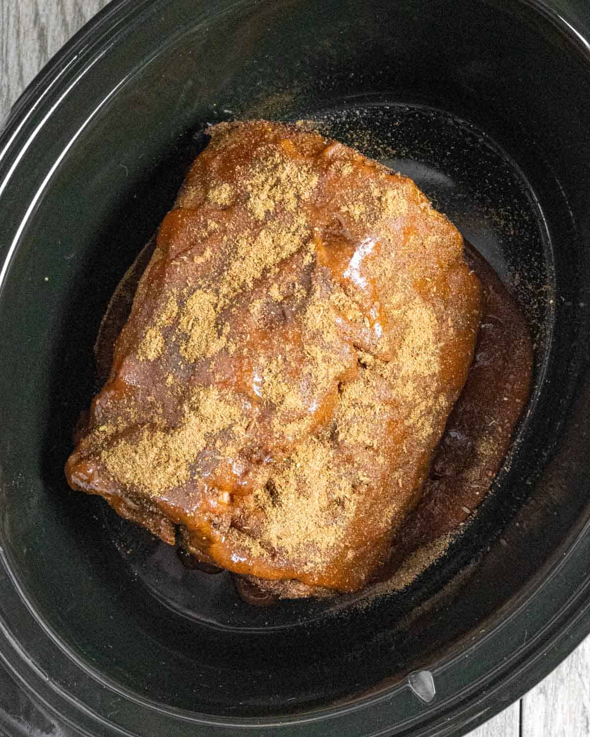 Browned pork shoulder roast set into the crock pot sprinkled with additional rub.