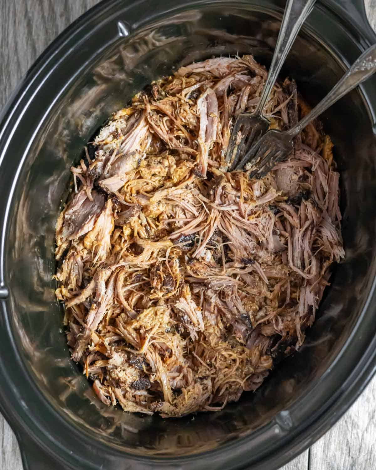 Freshly pulled pork shredded in the crock pot with two forks in the pot.