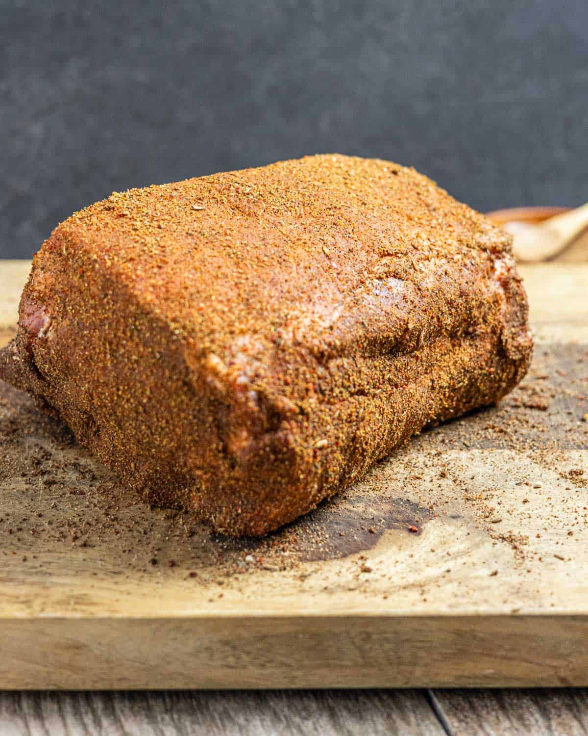 Raw pork shoulder on a wood board covered in dry spice rub.