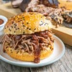 Pulled pork piled on a sesame seed bun with sauce dripping down the side.