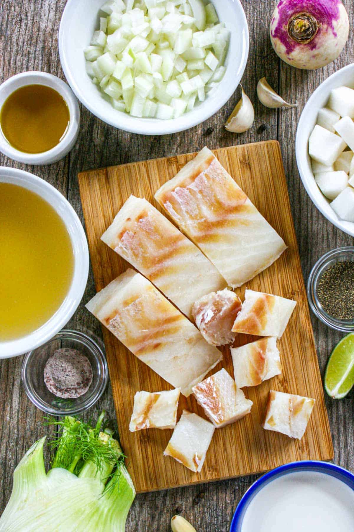 Fish stew ingredients in small bowls and a cutting board.