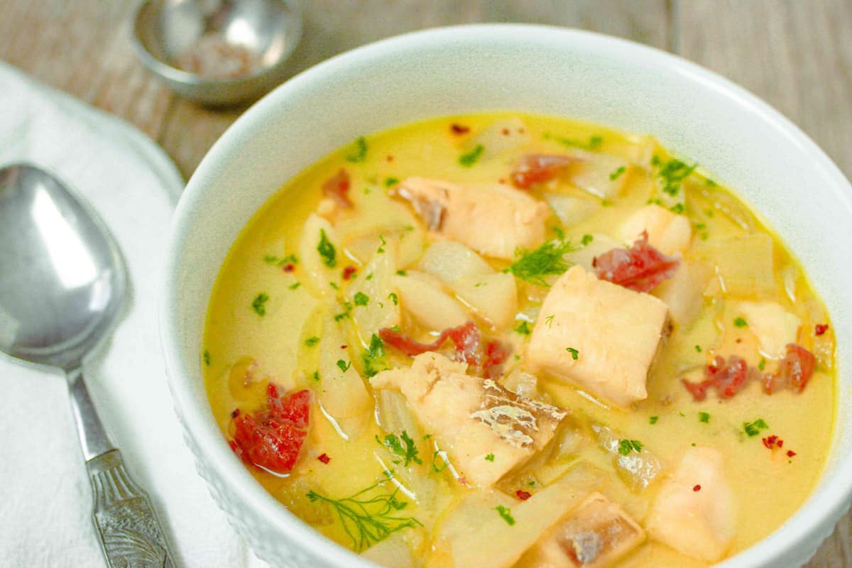 White bowl of fish stew showing chunks of fish and fennel tops as garnish.