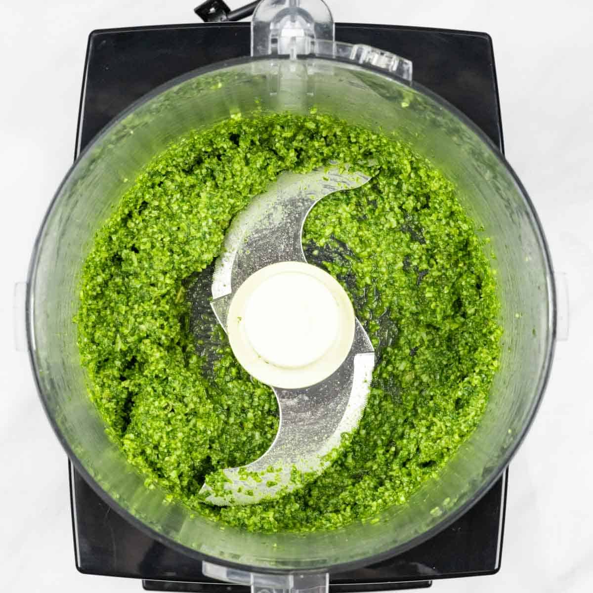 Looking into food processor bowl of blended nut-free pesto.