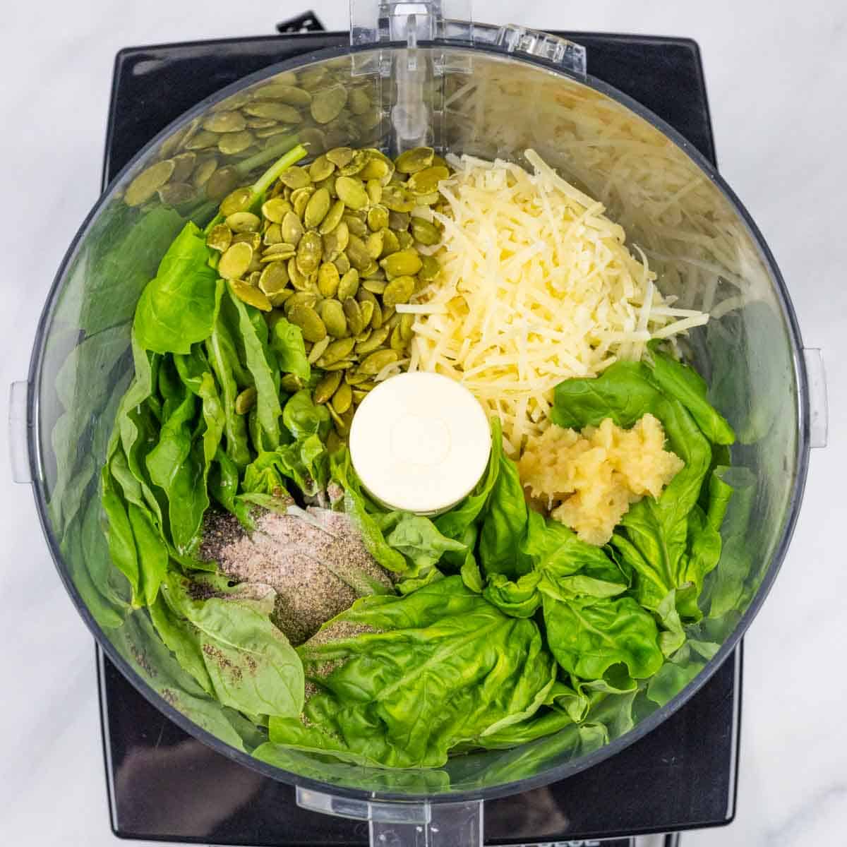 View into bowl of food processor of pesto ingredients in piles before blending.