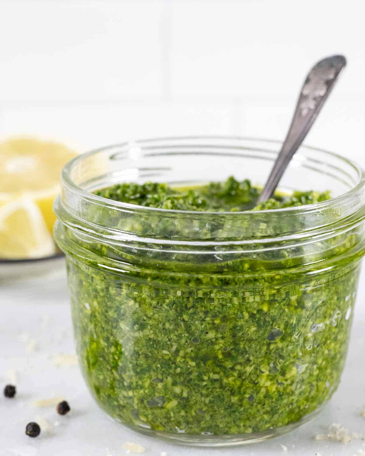 Side of small glass mason jar with pesto and a spoon in it.