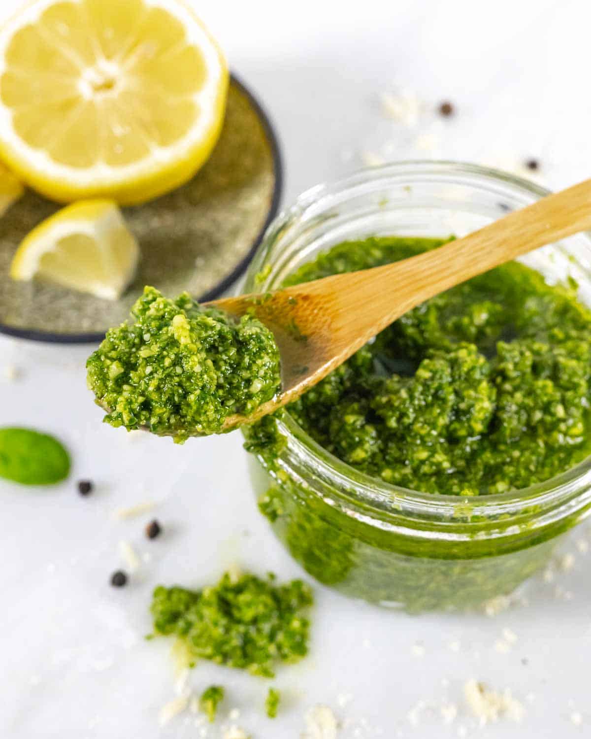 Jar of basil pesto with small wood spoonful laying across the top.