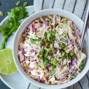 Coleslaw in a white bowl with a lime and cilantro garnish.