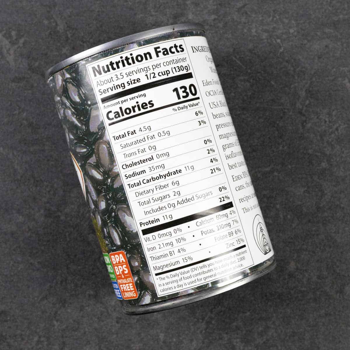 Can of black soy beans on its side on a grey board showing the nutrition label.