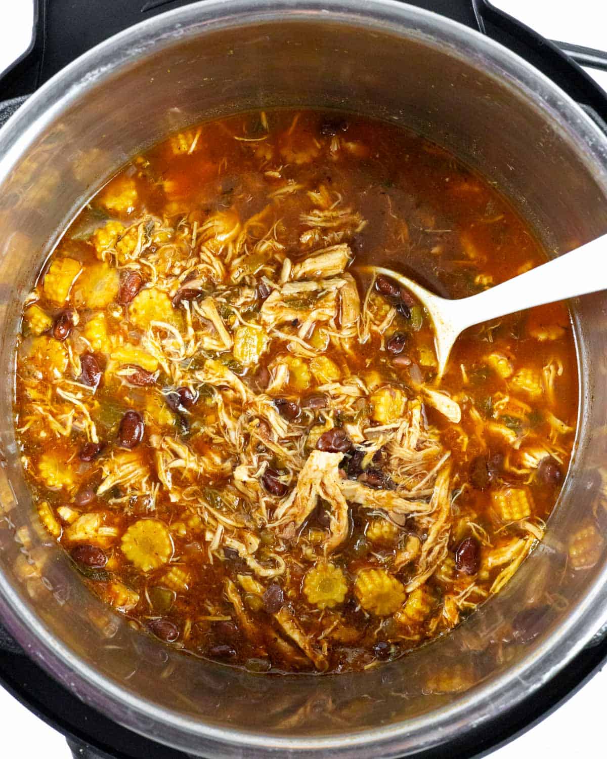 Finished pot of chicken taco soup with shredded chicken and a white spoon in the pot.