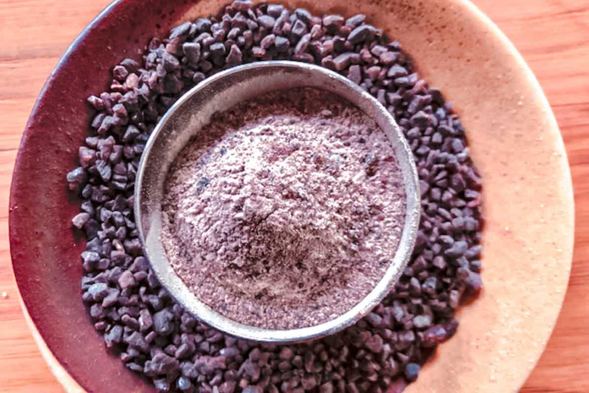 Coarse kala namak in earthenware saucer with a small salt bowl in the center filled with fine ground kala namak.