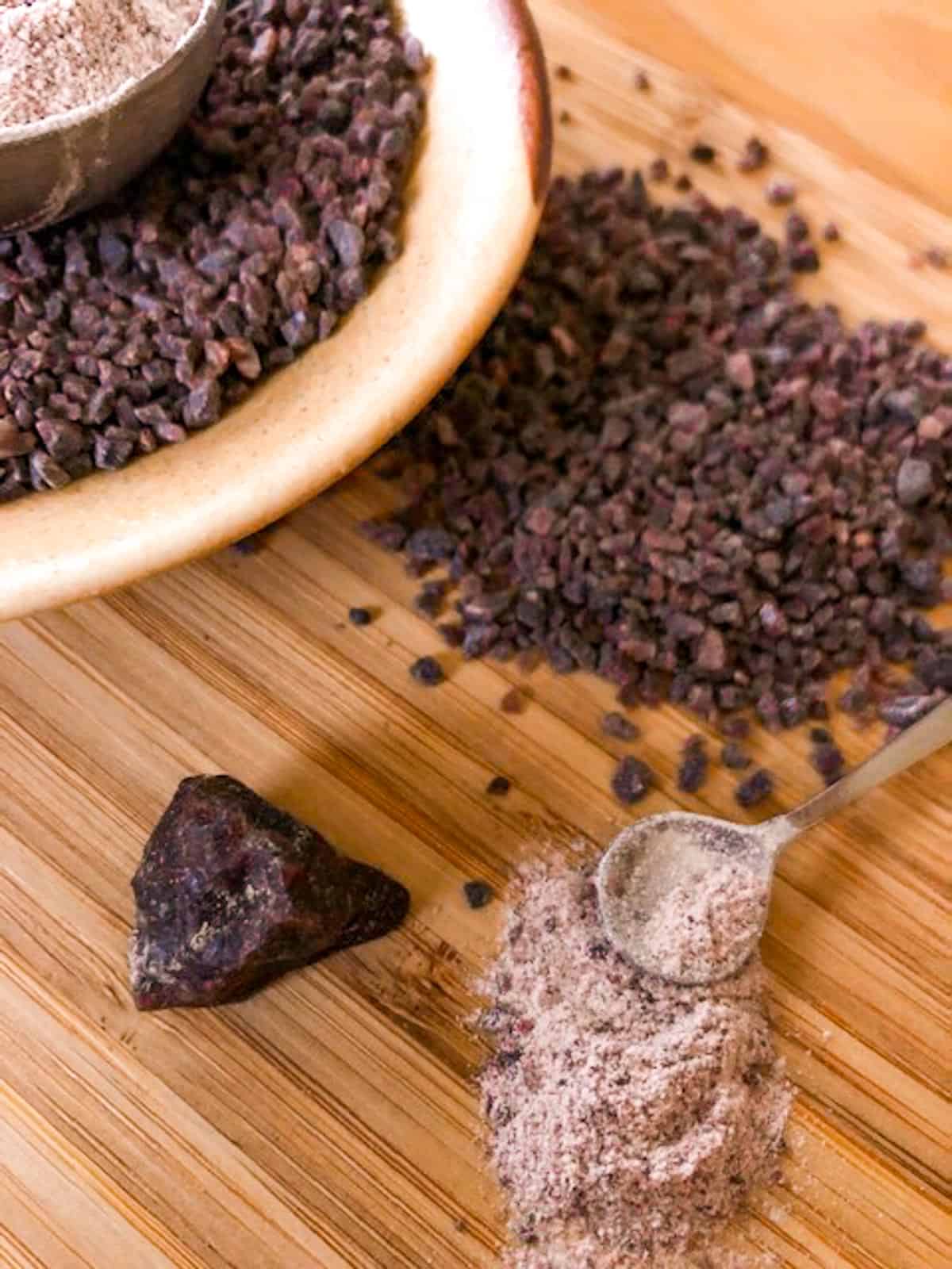 Coarse himalayan black salt on a wood board with a salt rock and salt spoon with fine ground kala namak.