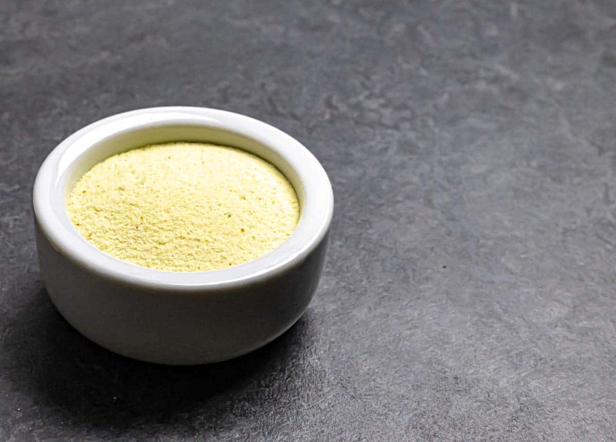 White bowl of powdered Asafoetida or Hing on a grey board.