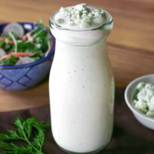 Blue cheese dressing in a glass dressing bottle with a side salad and bowl of gorgonzola cheese.