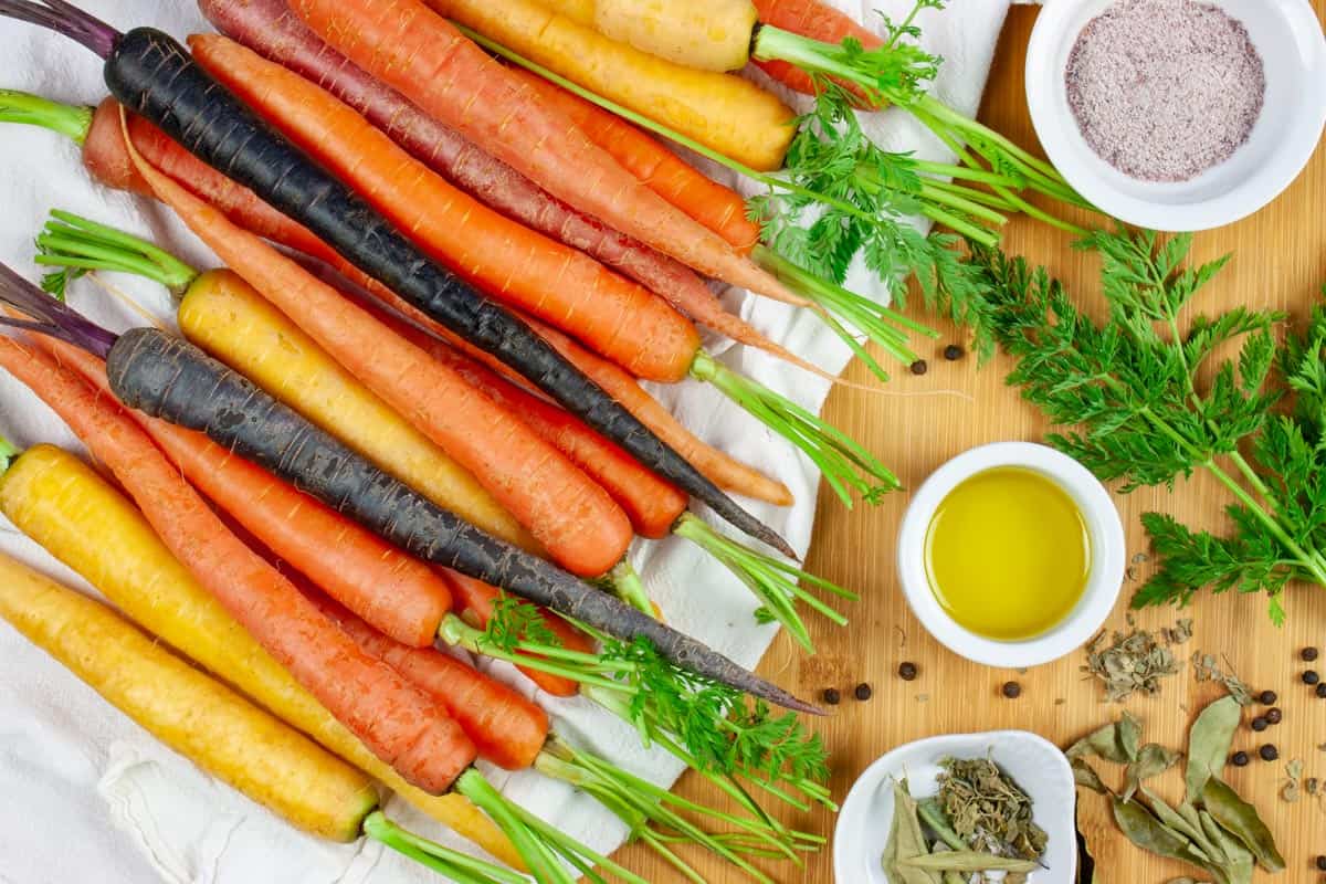 Stack of raw rainbow carrots on a white towel with ingredients in small white bowls.