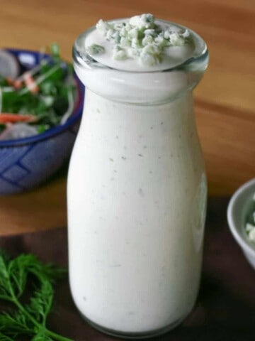 Blue cheese dressing in a glass dressing bottle with a side salad and bowl of gorgonzola cheese.