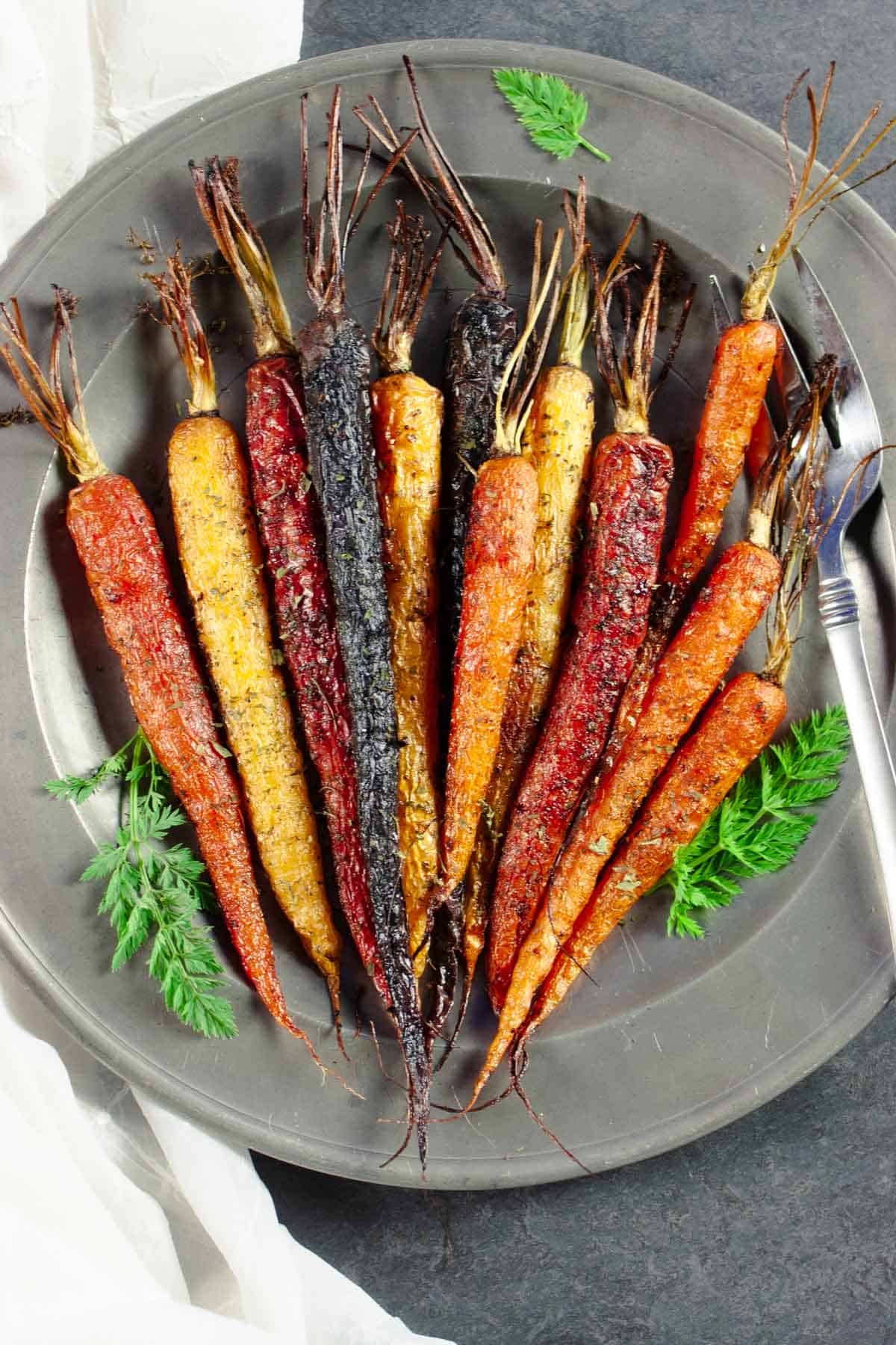 Roasted carrots on a silver plate with carrot top garnish and fork.