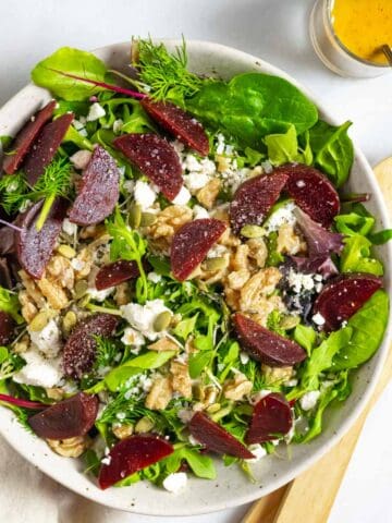 Beet and feta salad in a white bowl topped with walnuts and tahini dressing.