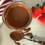 Dish of keto chocolate sauce with a dipped spoon on the side and three fresh strawberries.
