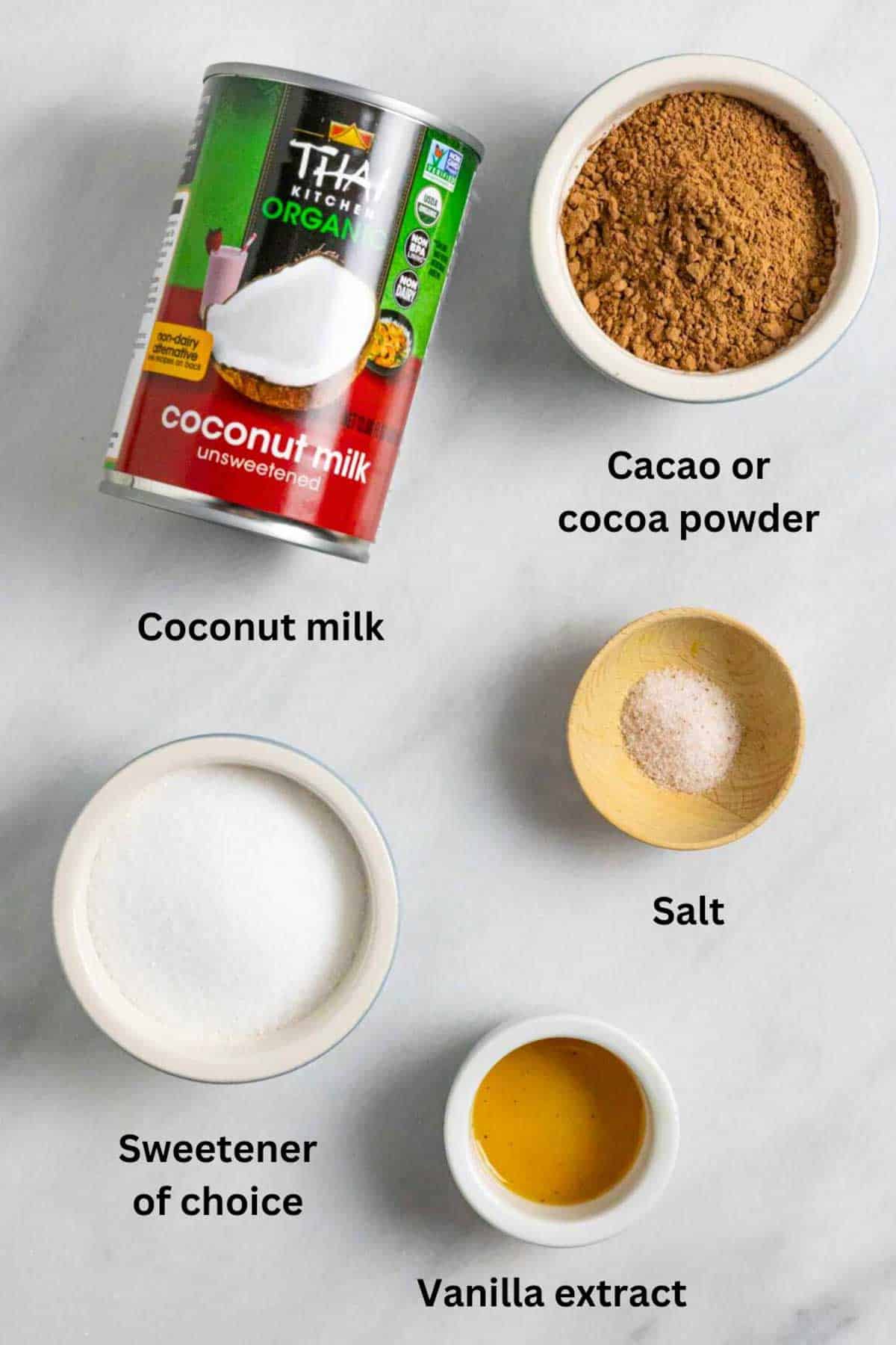 Ingredients for dairy-free chocolate sauce in small bowls on a marble board with black text labels.