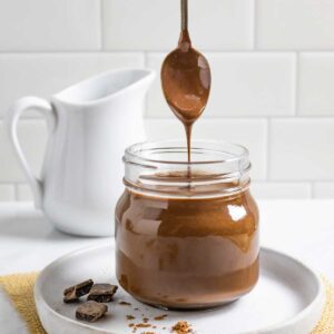 Jar of coconut milk chocolate sauce with a spoonful streaming into the jar.