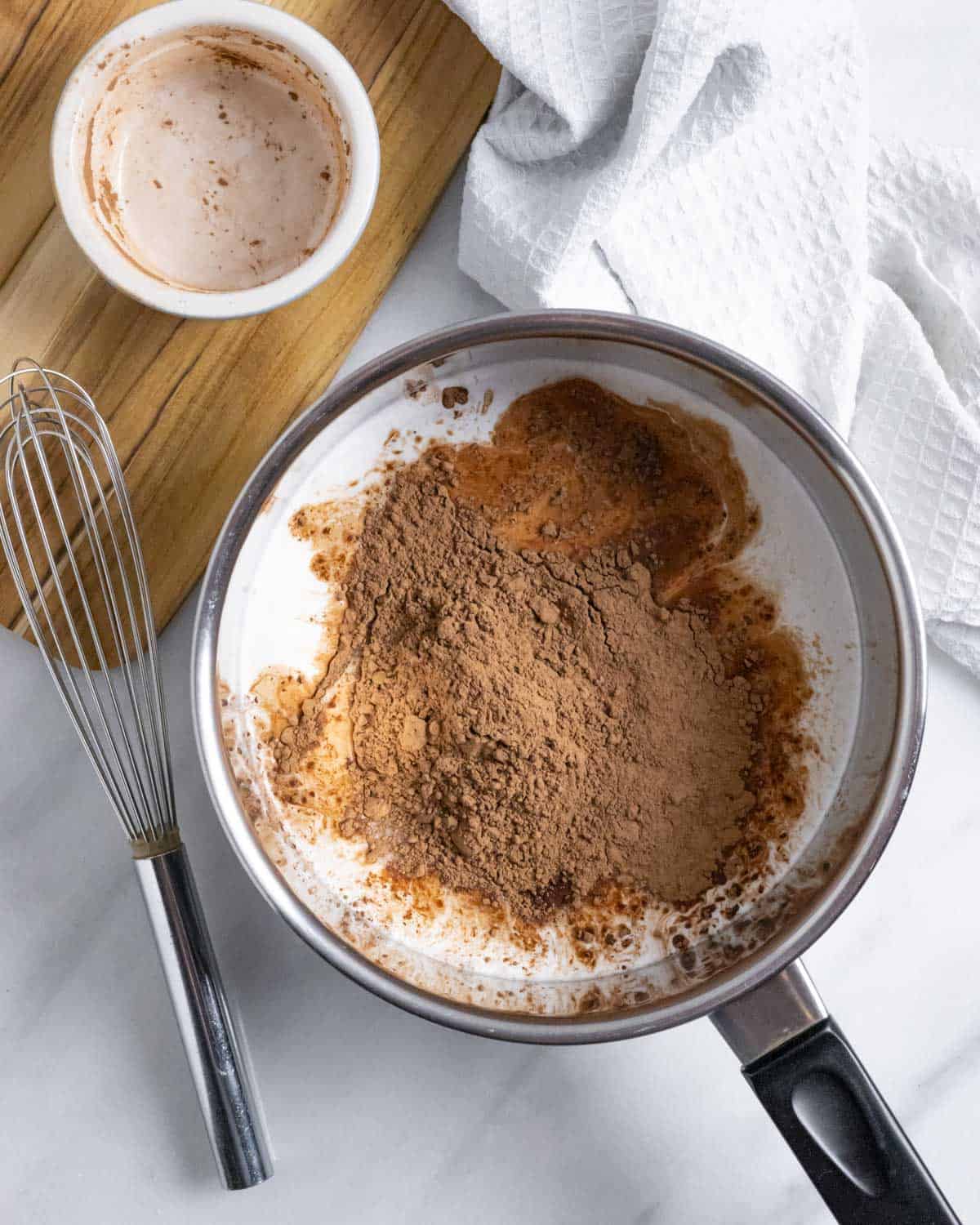 Saucepan with unmixed ingredients for keto chocolate sauce with a whisk next to it.