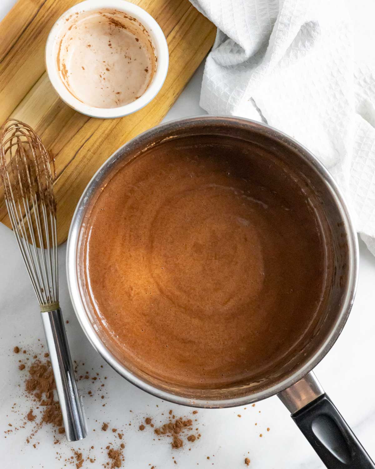 Simmered chocolate sauce in a saucepan with a whisk next to it.