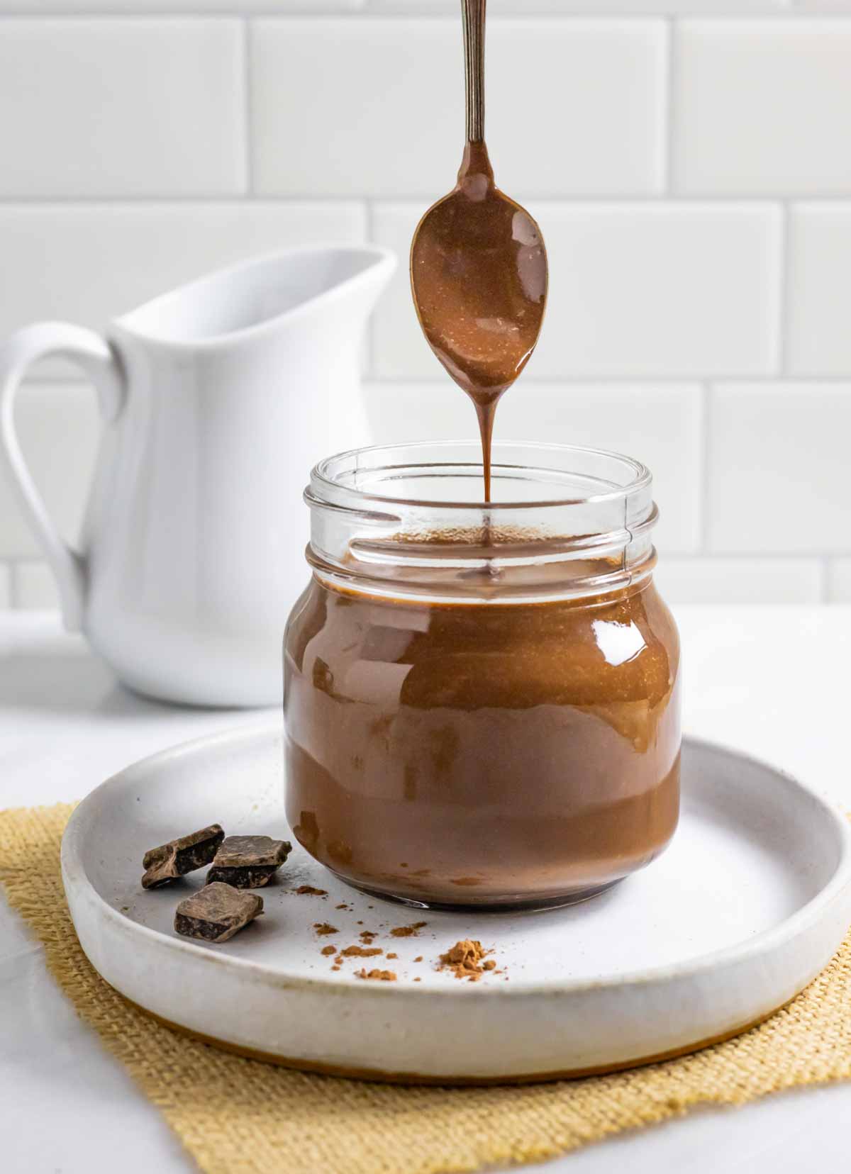 Jar of coconut milk chocolate sauce with a spoonful of a stream of dripping sauce pouring into the jar.