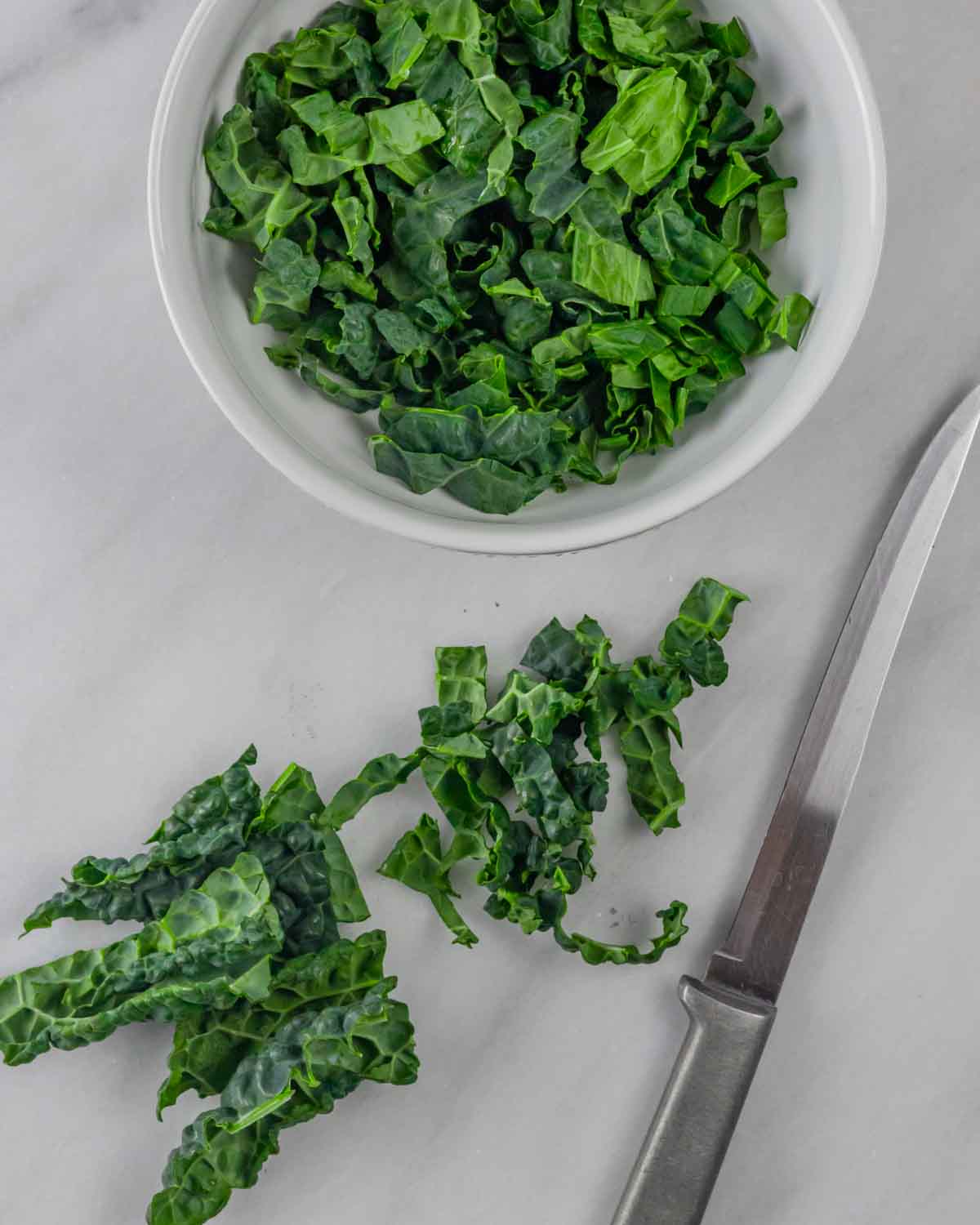 Chopped kale on cutting board with knife and bowl of kale.