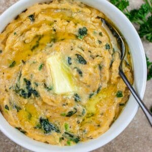 Keto colcannon in a white bowl topped with melted butter and a spoon with a parsley garnish.