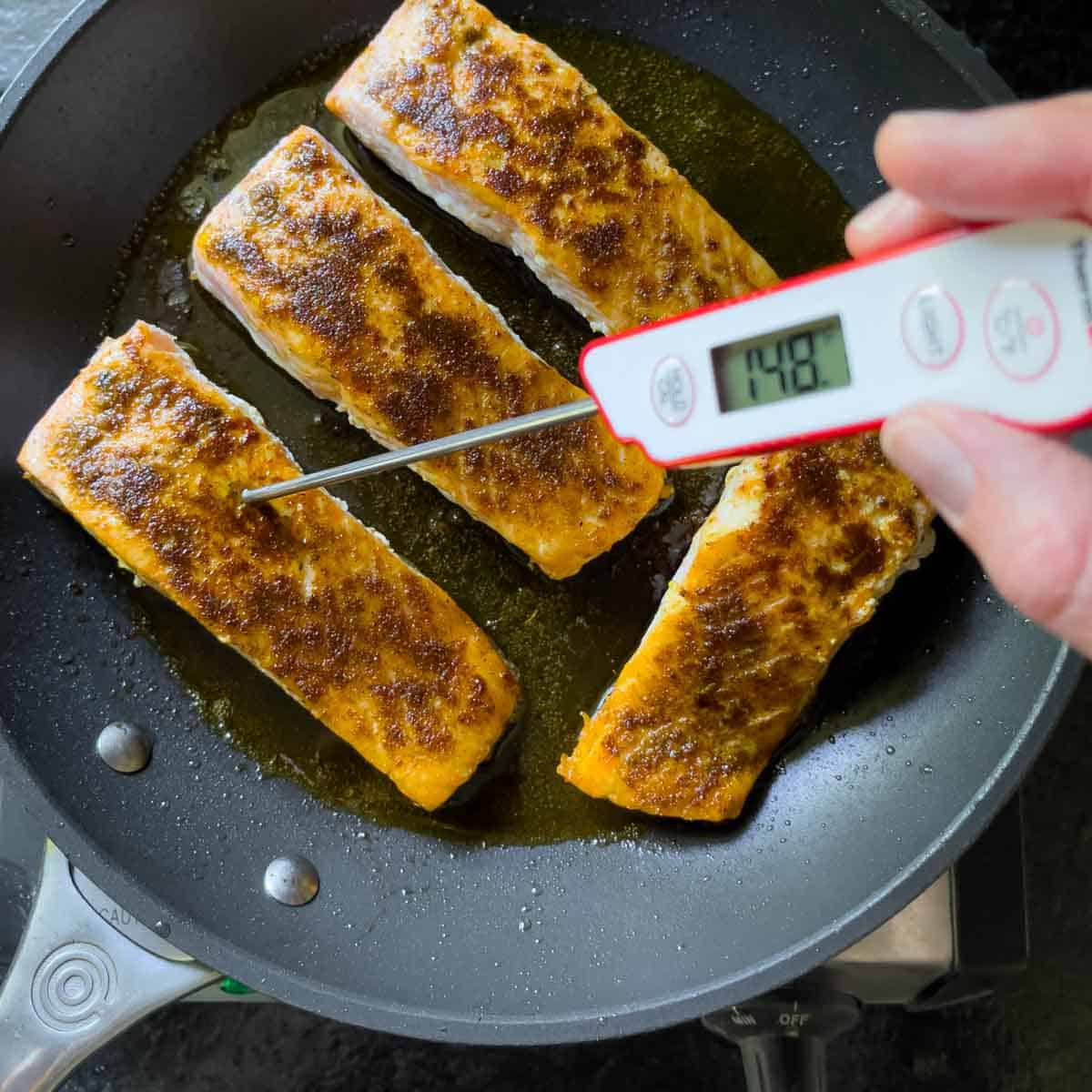 Seasoned fillets in a skillet with a meat thermometer temping one of them at 148 degrees.