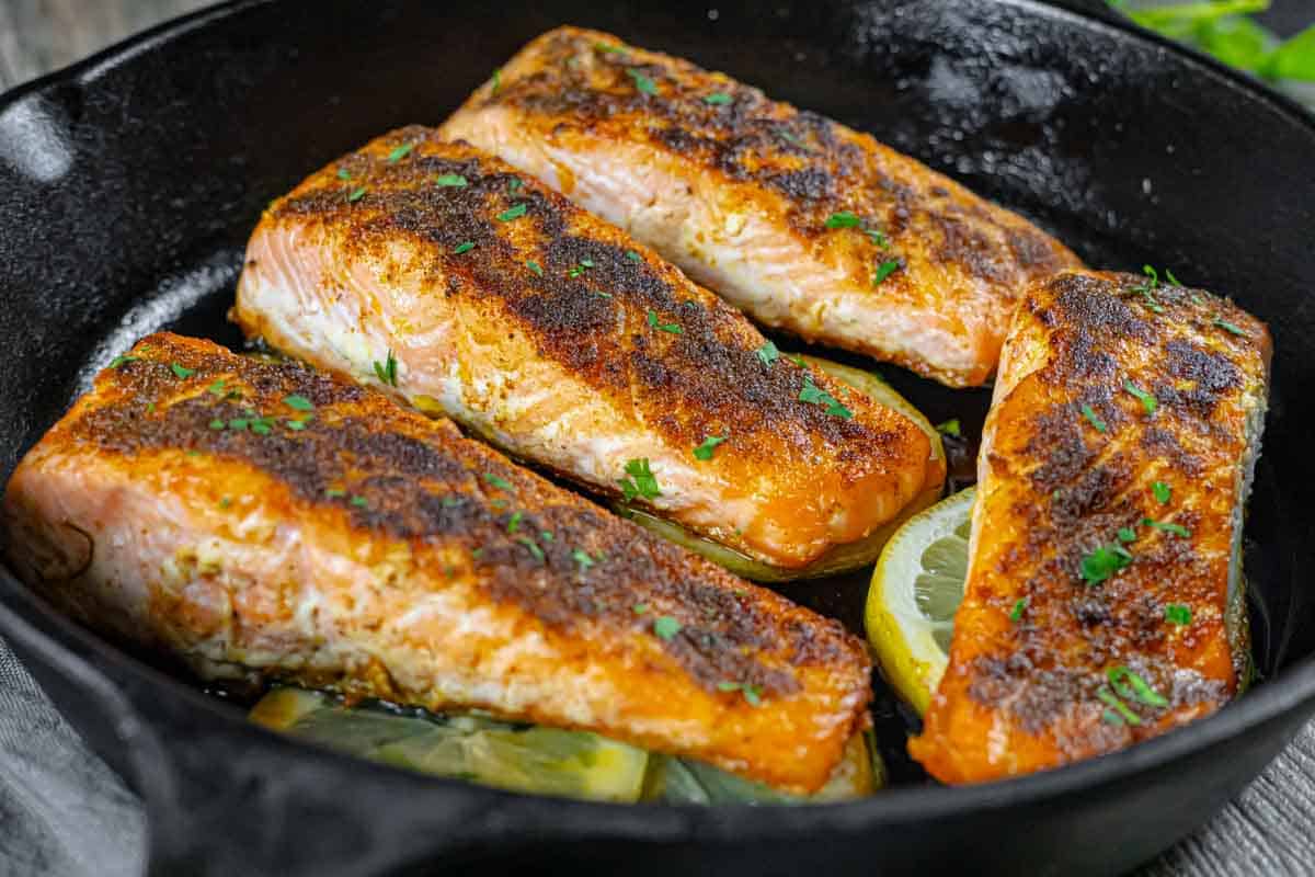 Pan-seared fillets of tikka spiced salmon on lemon slices in a cast iron skillet.