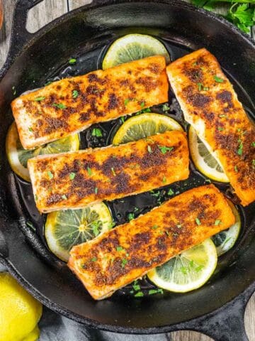 Tikka masala Indian spiced salmon fillets on a bed of lemon slices in a cast iron skillet.