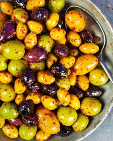 Marinated olives in a pewter bowl with a spoon.