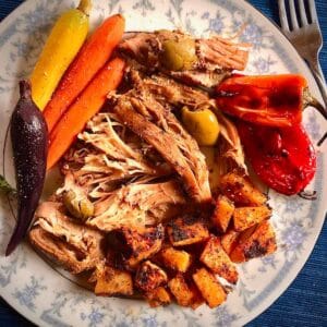 Meal of balsamic turkey thighs with olives and sides of herb roasted rutabgagas and carrots on a blue and white plate.