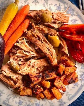 Meal of balsamic turkey thighs with olives and sides of herb roasted rutabgagas and carrots on a blue and white plate.