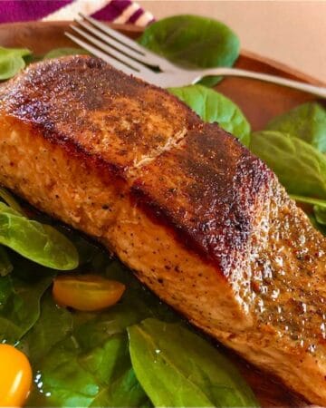 Seared salmon filet browned with spices on a bed of baby spinach with yellow grape tomatoes.