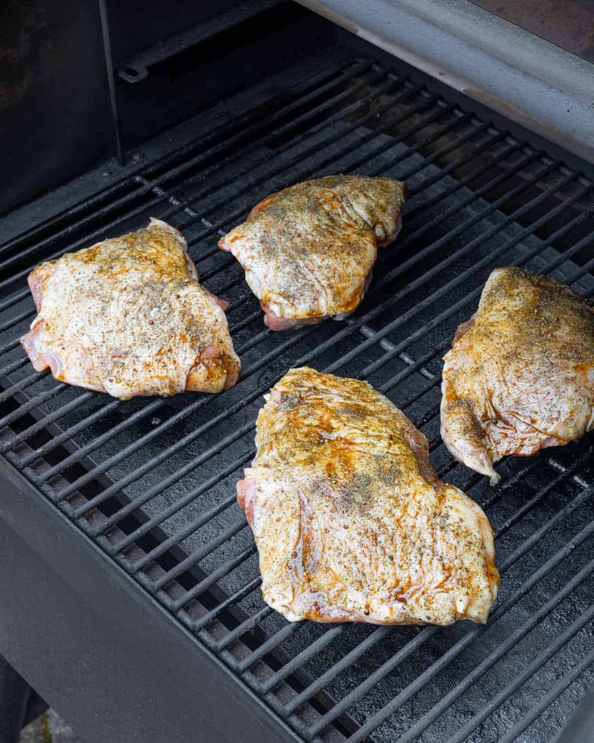 Four seasoned turkey thighs placed skin-side up on smoker grill grates.