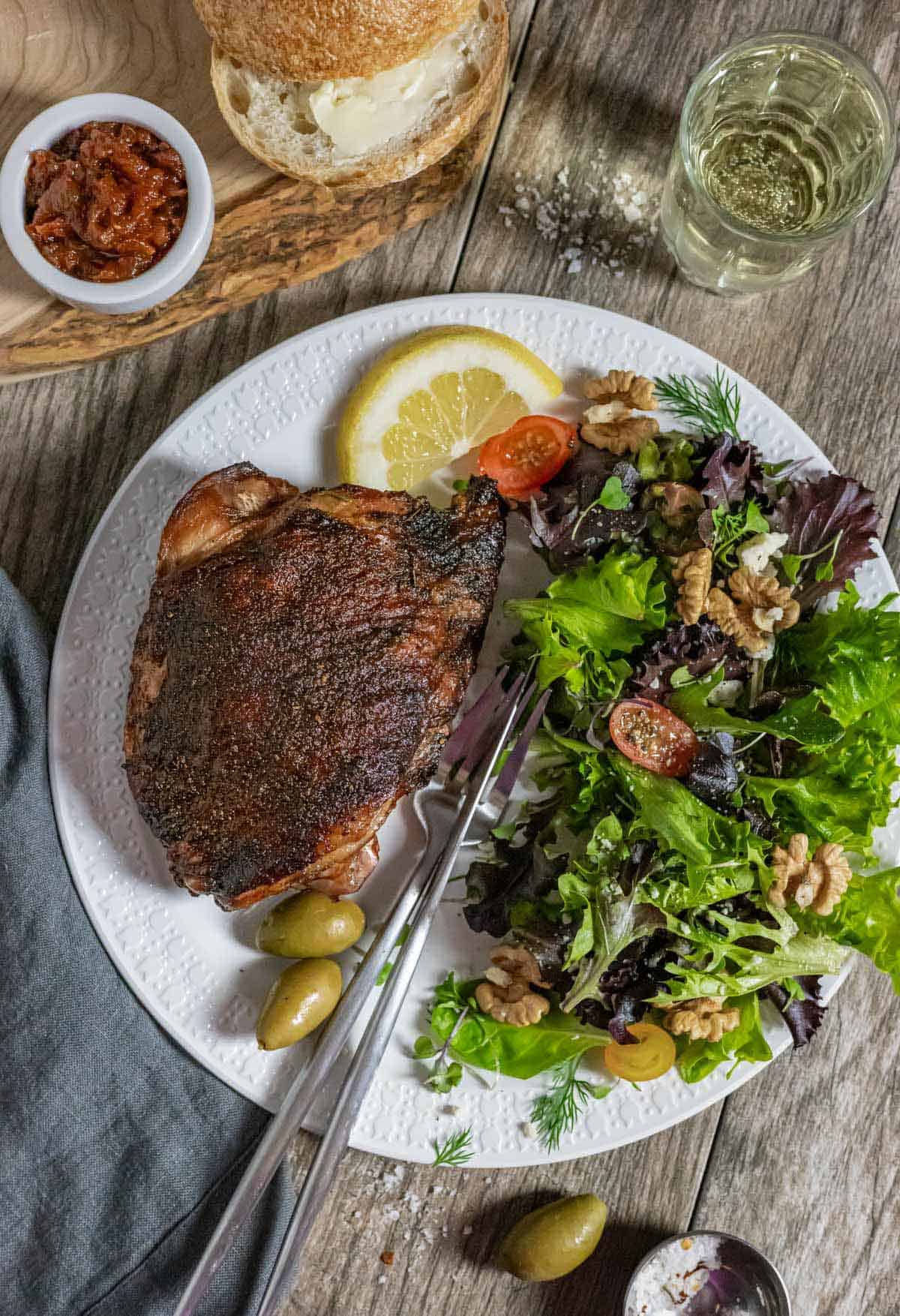 Smoked turkey thigh on a plate with green salad and olives.