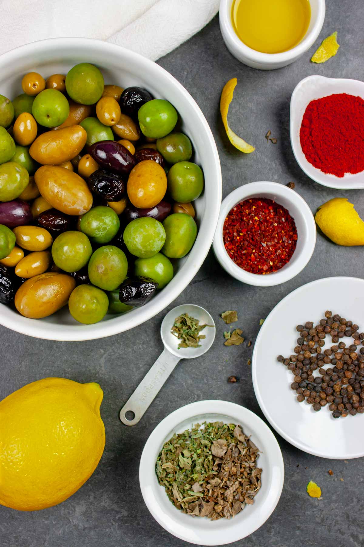 White bowls with marinated olives ingredients on a grey board.