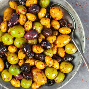 Marinated olives in a pewter bowl with a spoon.