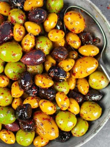 Marinated olives in a pewter bowl with a spoon.