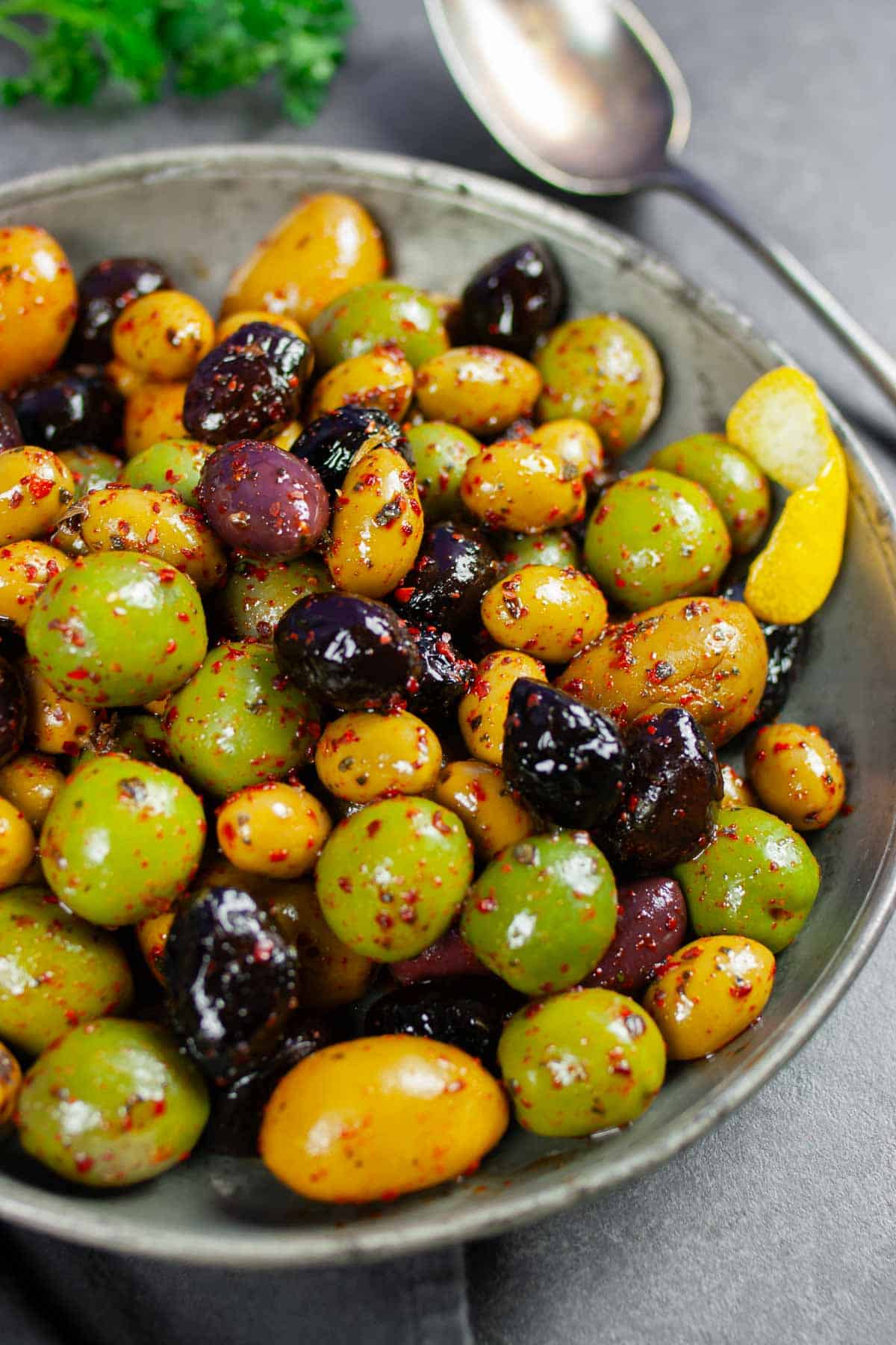 Spicy marinated olives of several varieties in a pewter serving dish sprinkled with Aleppo pepper.