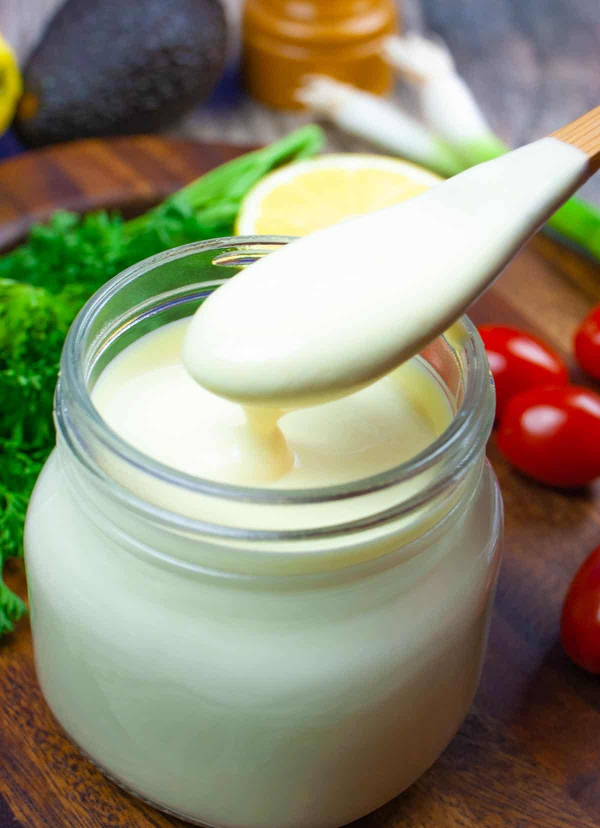 Small mason jar of lemon dressing with small wooden spoon of dressing dripping back into the jar.