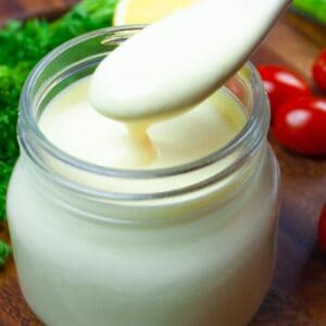 Close up of small mason jar of lemon dressing with small wooden spoon of dressing dripping back into the jar.