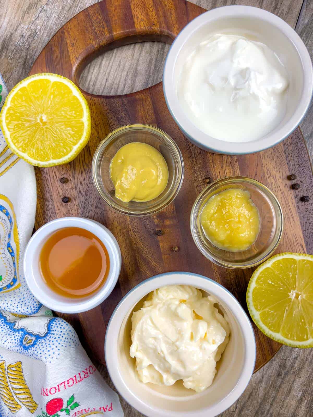 Overhead view of  creme fraiche dressing ingredients in small ramekins on an oval wood cutting board.