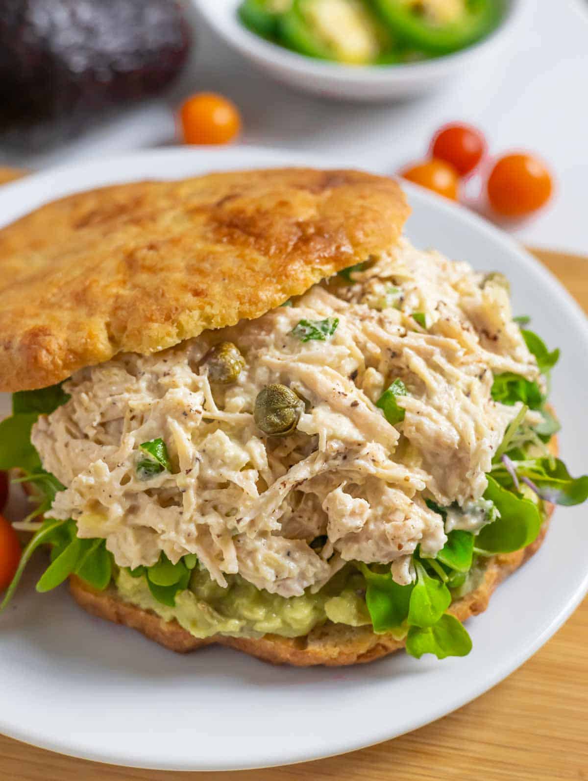 Spicy chicken salad on a sandwich thin with sprouts and avocado.